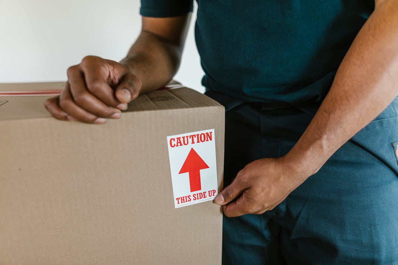 about-us-01 A person handling a moving box with a 'caution this side up' label indoors.
